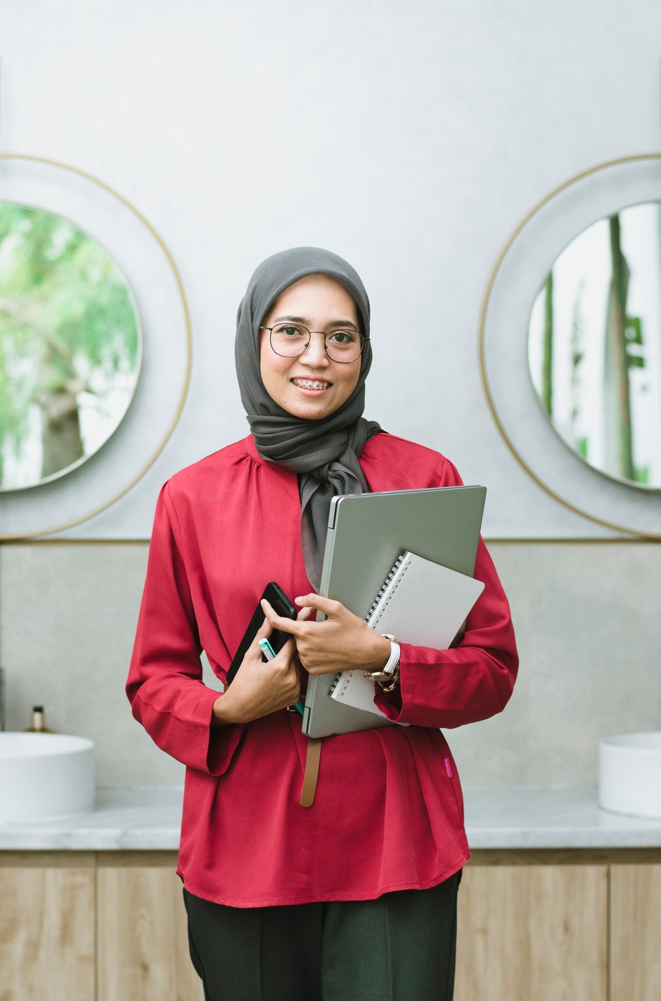 Woman Holding a Smartphone, Laptop, and Notebook in the Bathroom